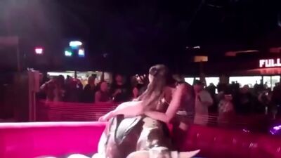 Девушка в коротеньком платье катается на механическом быке